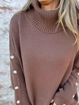 Woman wearing a dark brown ribbed turtleneck sweater with decorative button sleeves and jeans.