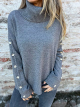 Woman wearing a dark gray ribbed turtleneck sweater with decorative button sleeves and jeans.