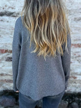 Woman wearing a dark gray ribbed turtleneck sweater with decorative button sleeves and jeans.