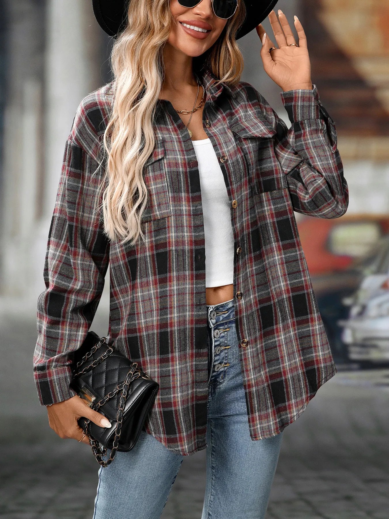 Woman wearing a dark gray plaid oversized button-up shirt layered over a white top with jeans and black crossbody bag.