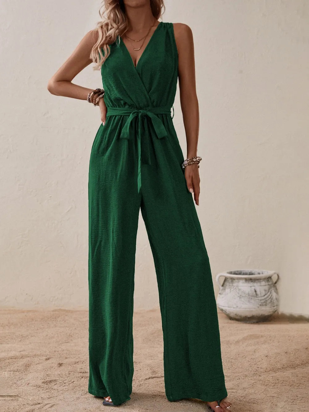Woman wearing the Honey Tied Surplice Sleeveless Wide Leg Jumpsuit in dark green with a tie waist and wide-leg silhouette, elegant women's one-piece outfit from Chic Mystik Boutique.