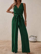 Woman wearing the Honey Tied Surplice Sleeveless Wide Leg Jumpsuit in dark green with a tie waist and wide-leg silhouette, elegant women's one-piece outfit from Chic Mystik Boutique.
