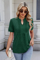 Woman wearing a dark green notched short-sleeve top with light-wash jeans, sunglasses, and layered jewelry.