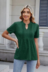 Woman wearing a dark green notched short-sleeve top with light-wash jeans, sunglasses, and layered jewelry.
