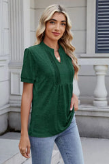 Woman wearing a dark green notched short-sleeve top with light-wash jeans, sunglasses, and layered jewelry.