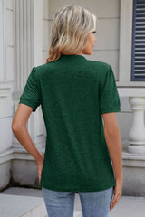 Woman wearing a dark green notched short-sleeve top with light-wash jeans, sunglasses, and layered jewelry.