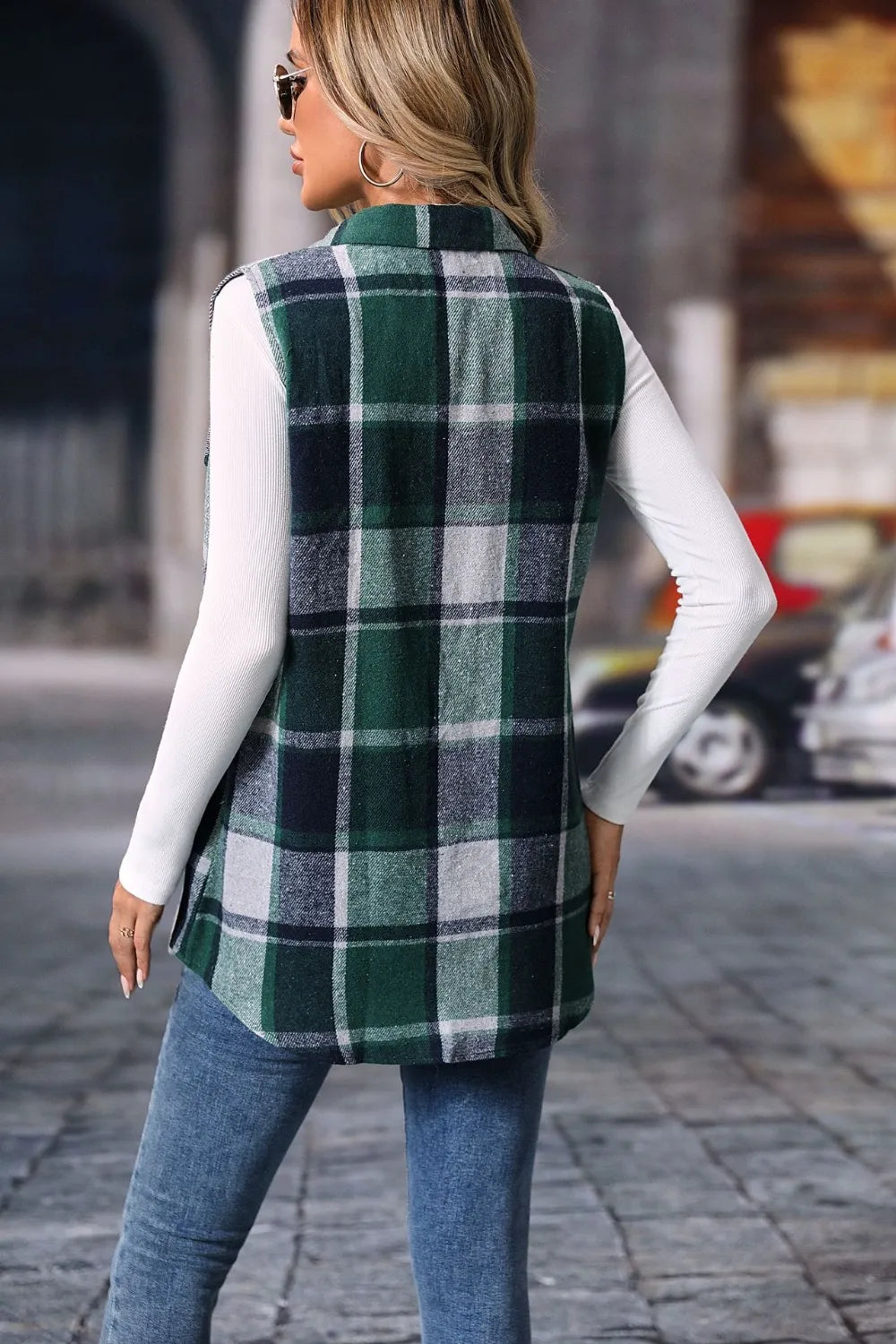 Woman wearing a dark green plaid button-up vest coat layered over a white turtleneck with blue jeans and gold jewelry for a cozy fall outfit.