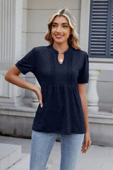 Woman wearing a dark navy notched short-sleeve top with light-wash jeans, sunglasses, and layered jewelry.