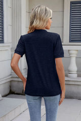 Woman wearing a dark navy notched short-sleeve top with light-wash jeans, sunglasses, and layered jewelry.