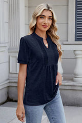 Woman wearing a dark navy notched short-sleeve top with light-wash jeans, sunglasses, and layered jewelry.
