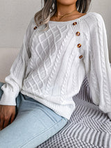 Woman wearing a white cable-knit sweater with decorative buttons, paired with light-wash jeans, layered gold necklaces, and a white handbag. Perfect for cozy fall and winter outfits.