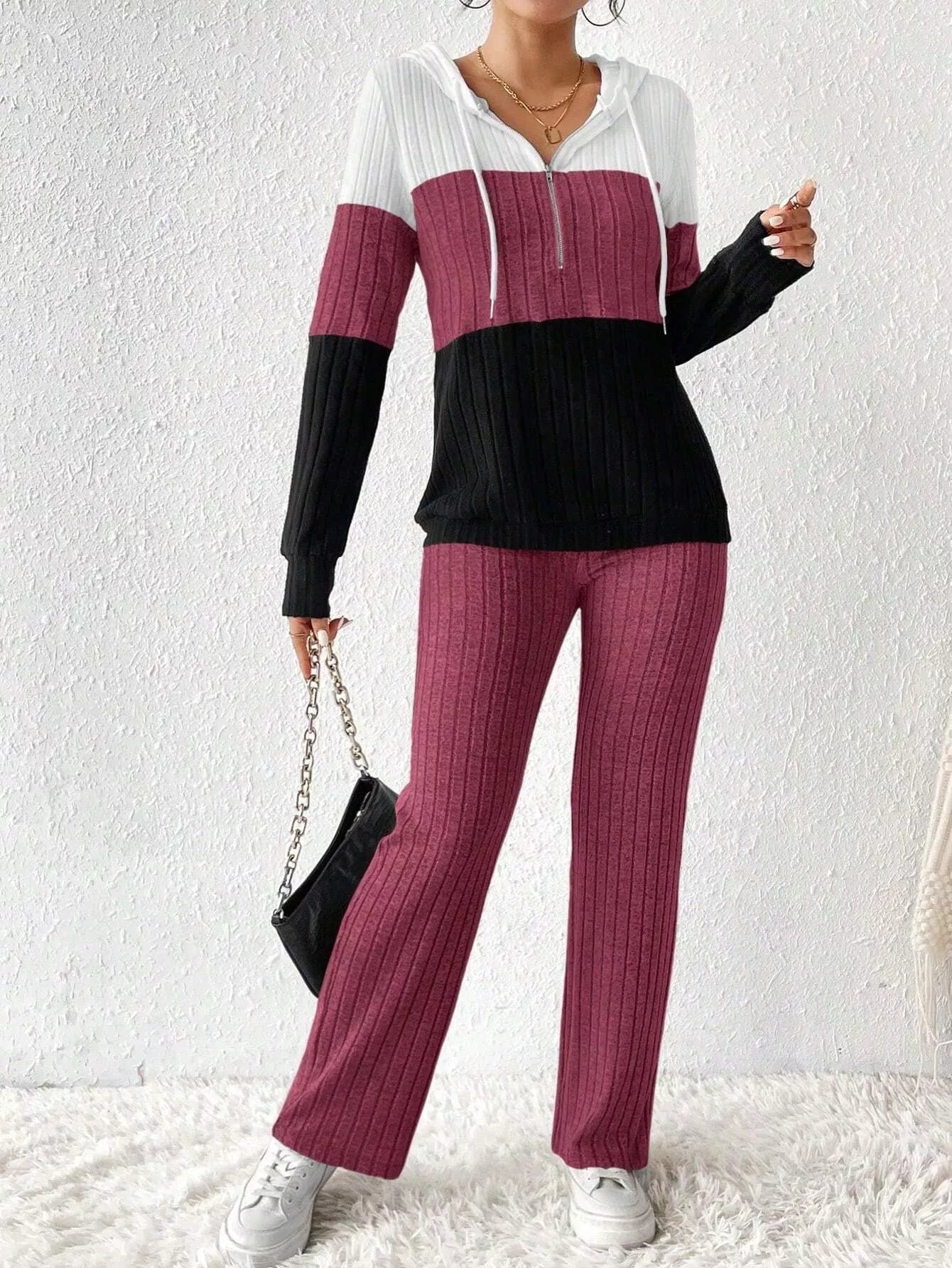 Woman wearing a deep purple, black and white color block half zip hooded top with matching ribbed-look pants.