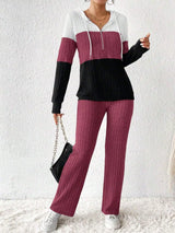 Woman wearing a deep purple, black and white color block half zip hooded top with matching ribbed-look pants.