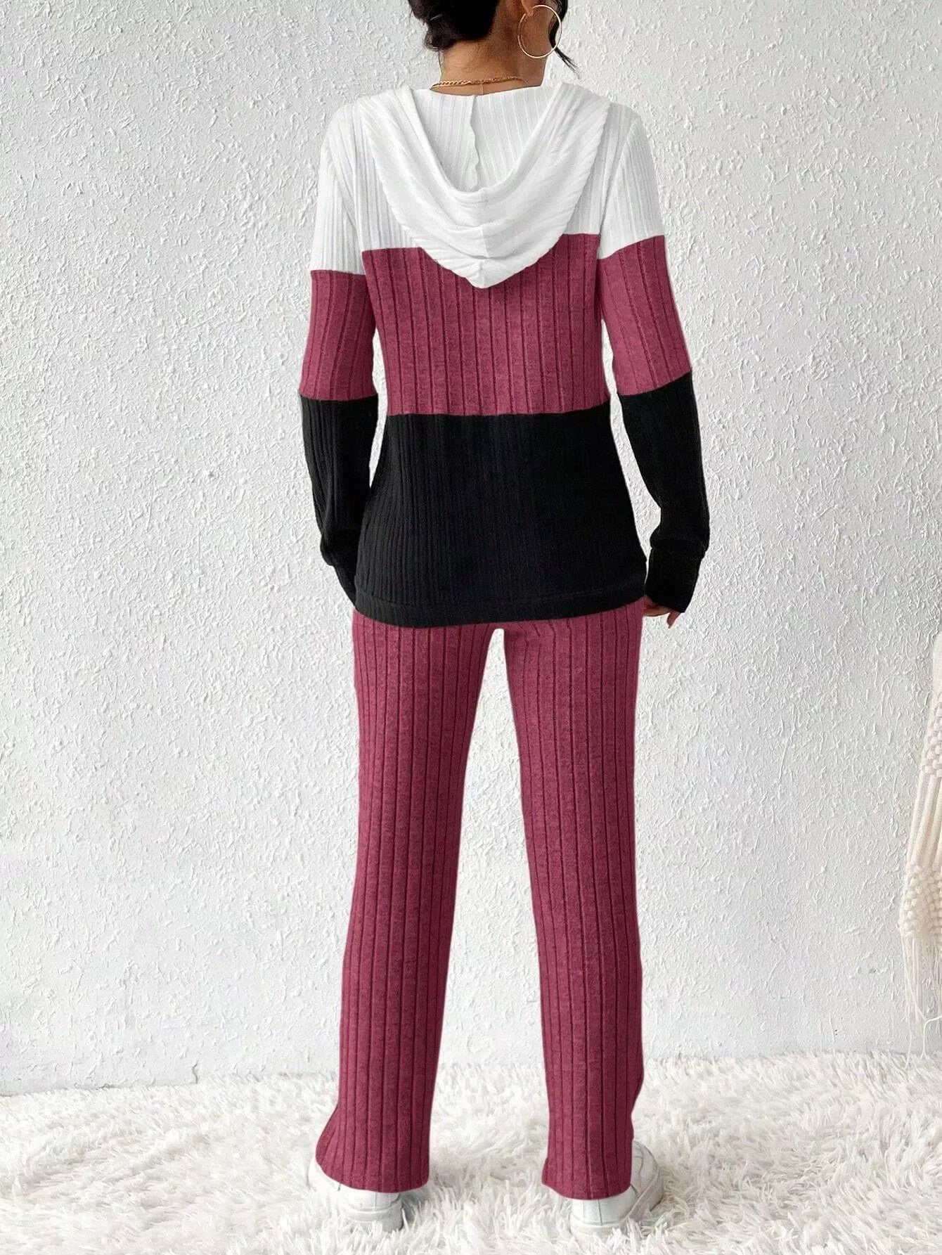 Woman wearing a deep purple, black and white color block half zip hooded top with matching ribbed-look pants.