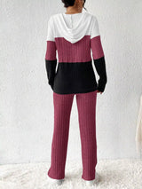 Woman wearing a deep purple, black and white color block half zip hooded top with matching ribbed-look pants.