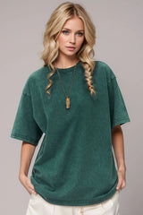 Woman wearing an oversized deep teal Basic Bae round-neck half-sleeve T-shirt styled with dark denim jeans and a long pendant necklace for a relaxed, casual look.