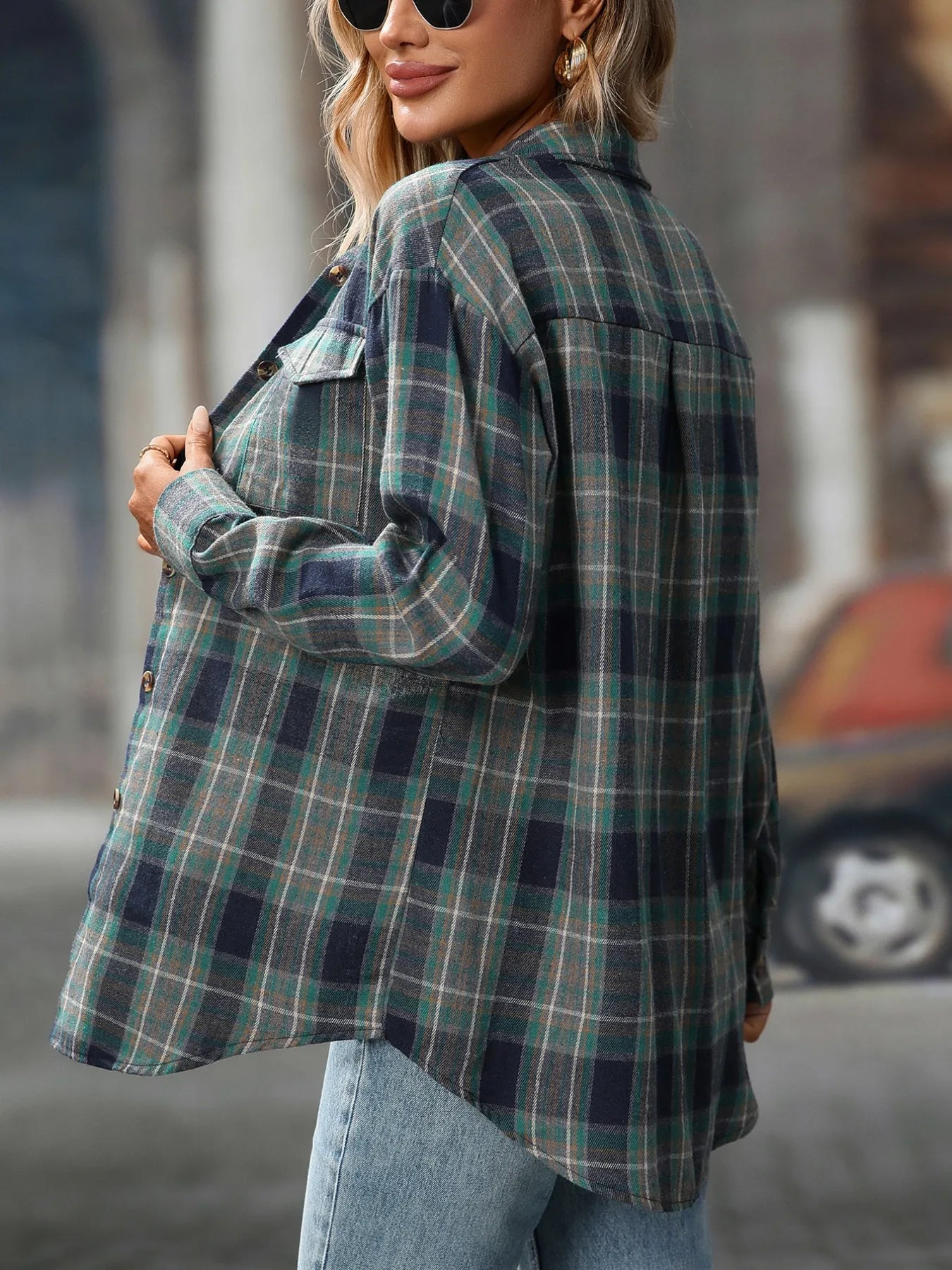 Woman wearing a deep teal plaid oversized button-up shirt layered over a white top with jeans and black crossbody bag.