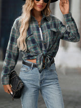 Woman wearing a deep teal plaid oversized button-up shirt layered over a white top with jeans and black crossbody bag.