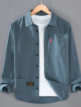 Men’s denim blue plus size button-up long sleeve shirt with multiple pockets, shown layered over a white T-shirt.