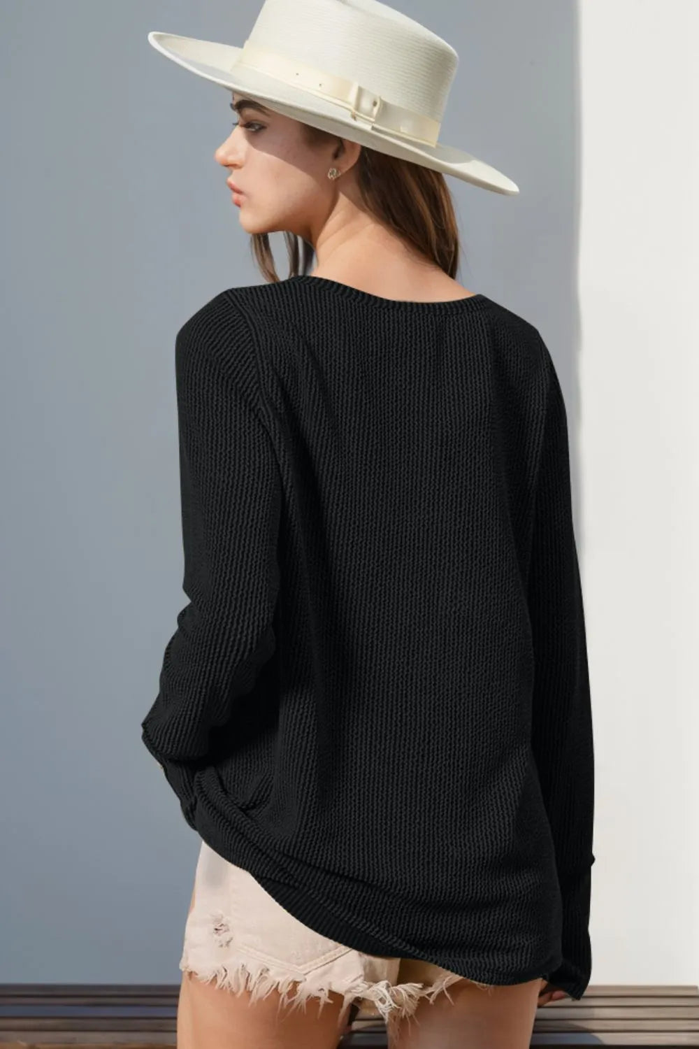 Person wearing a black sweater and white hat against a gray wall
