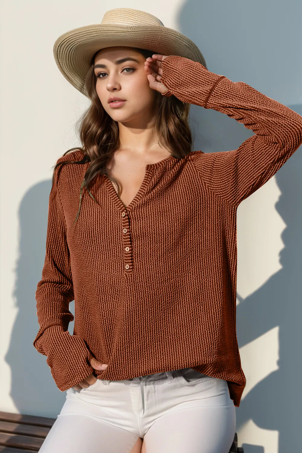 Woman wearing a brown knitted sweater and straw hat against a light background