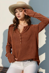 Woman wearing a brown knitted sweater and straw hat against a light background