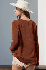 Woman wearing a brown sweater and white hat against a gray wall.