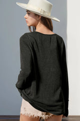 Woman wearing a dark gray textured sweater and white hat against a gray wall.