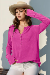 Woman wearing a fuchsia pink sweater and straw hat against a light background