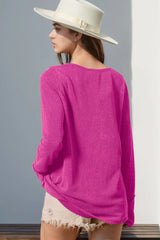 Person wearing a fuchsia pink sweater and white hat against a gray wall.