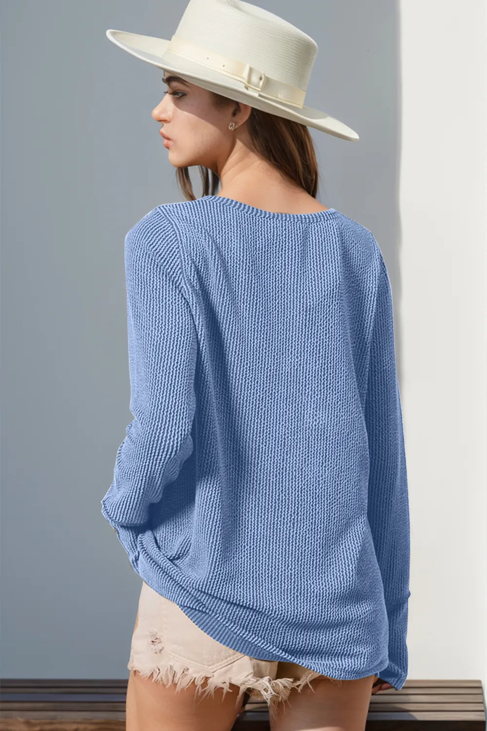 Person wearing a light blue sweater and white hat against a gray wall.