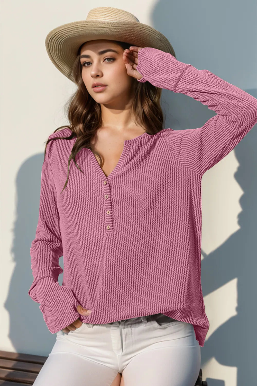 Woman wearing a pink knitted sweater and straw hat against a light background