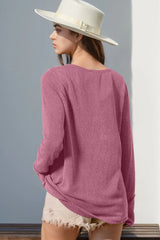 Woman wearing a pink sweater and white hat against a gray wall.