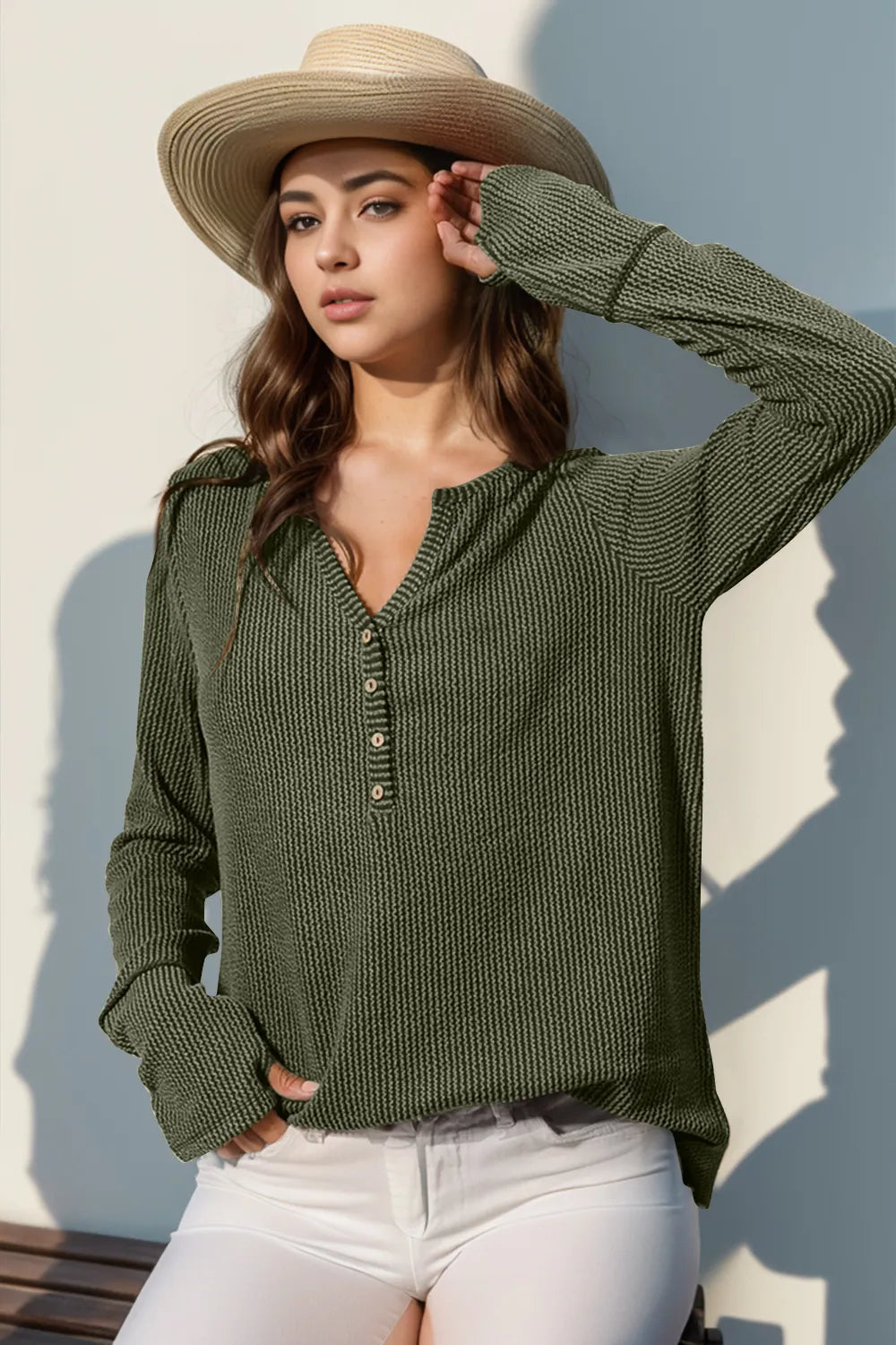 Woman wearing a green sweater and straw hat against a light background