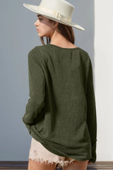 Person wearing a green sweater and white hat against a gray wall showing back of shirt.