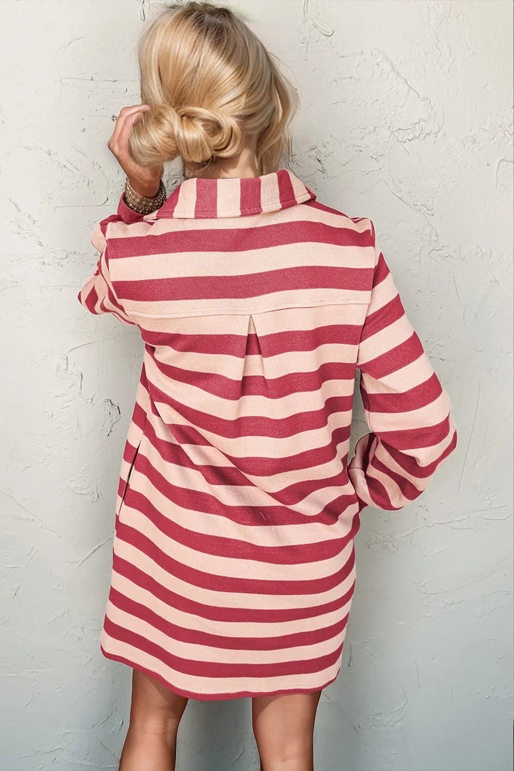 Person wearing a red and white striped dress against a textured white wall.