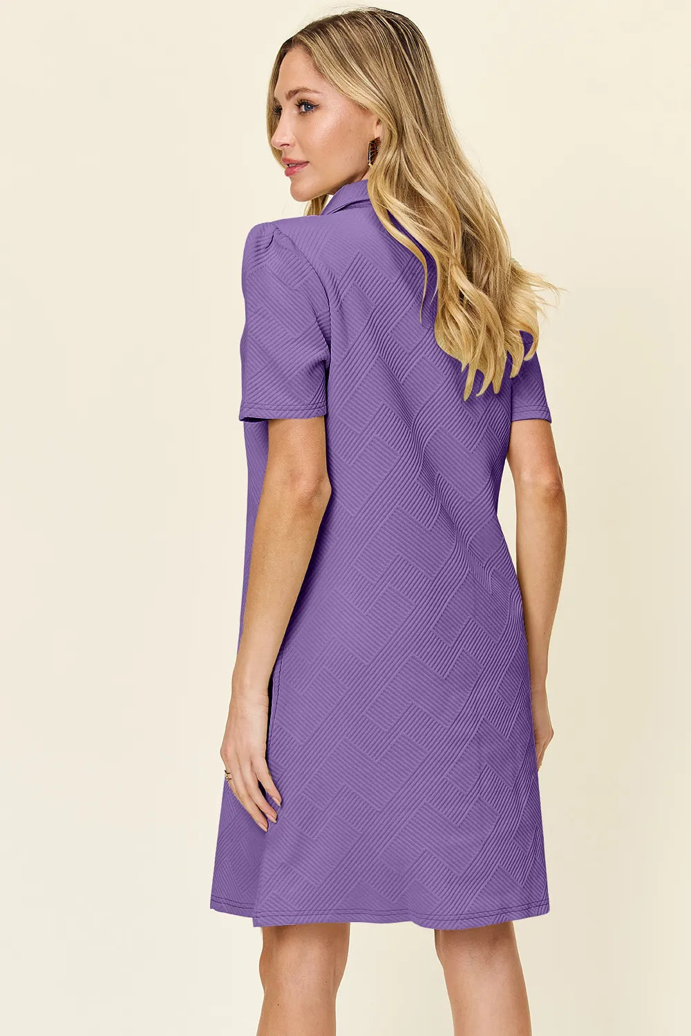 Woman wearing a purple dress against a beige background showing the back of the dress