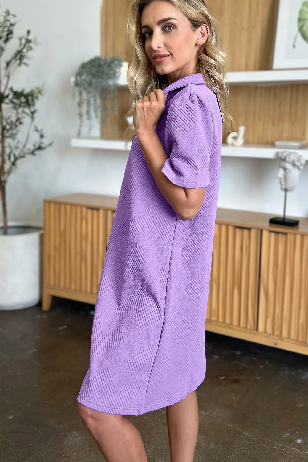 Woman wearing a purple dress in an indoor setting with wooden cabinets and decor showing the side of the dress.