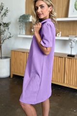 Woman wearing a purple dress in an indoor setting with wooden cabinets and decor showing the side of the dress.