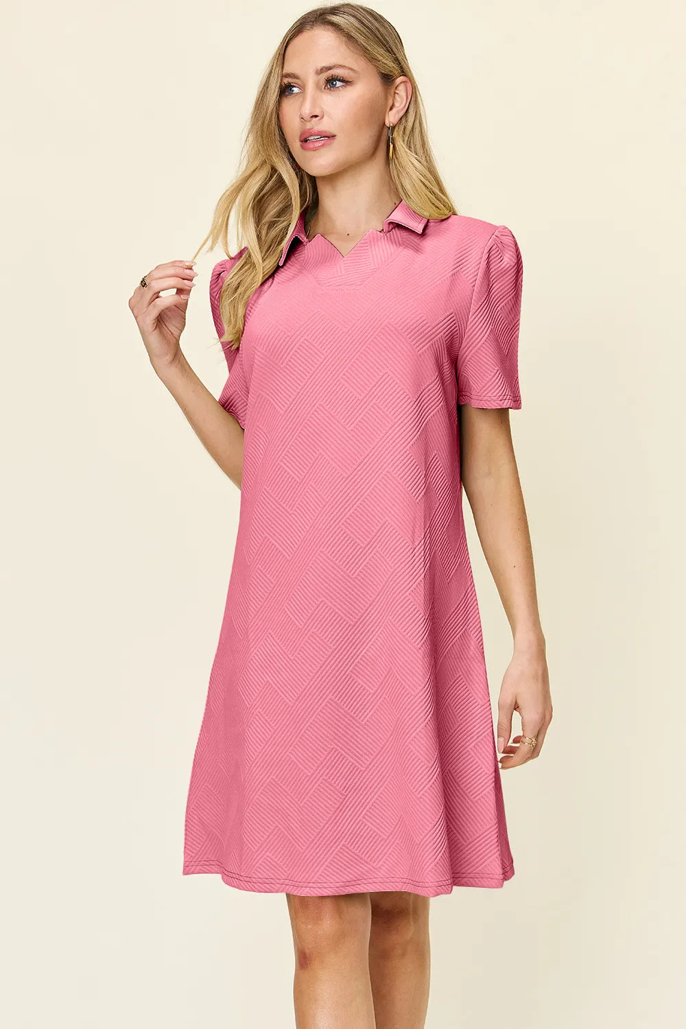 Woman wearing a pink dress with a collar on a beige background