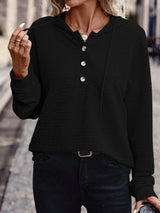Woman wearing a black textured drawstring quarter-button long sleeve hoodie paired with black jeans, perfect for casual fall outfits, available in 10 colors and sizes Small–2XL.