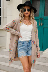 Woman wearing a dust storm open-front cardigan with colorful star print, front pockets, denim shorts and black Western boots.