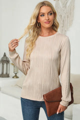Woman wearing a dust storm textured round neck long sleeve blouse with dark-wash jeans and brown clutch.
