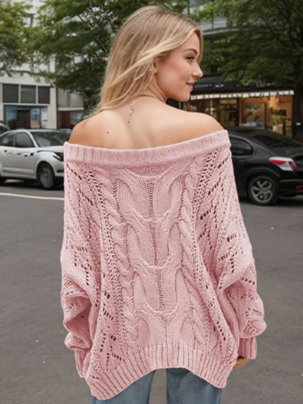 Woman wearing a dusty pink cable knit openwork off-shoulder sweater with distressed jeans and a wide-brim hat.