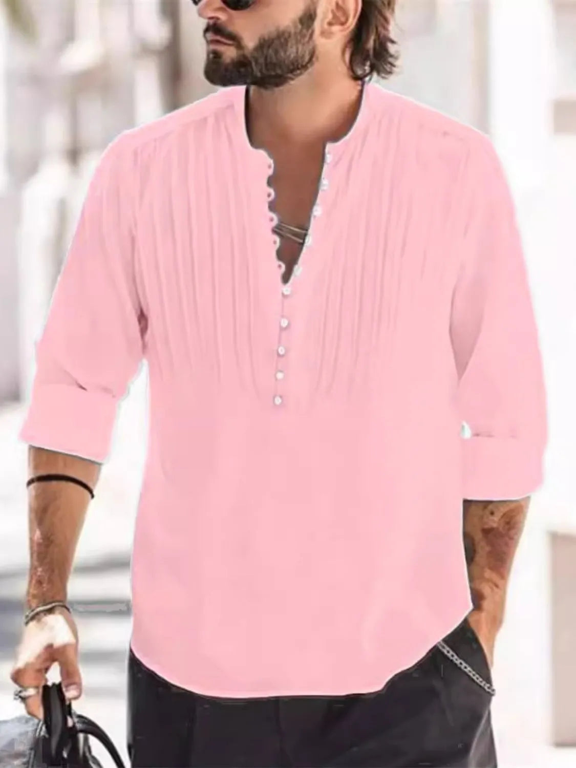 Man wearing a dusty pink button-detail long sleeve cotton polo with rolled sleeves and black pants.