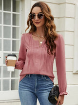 Woman wearing a dusty pink notched neck long sleeve blouse with flounce cuffs styled with light-wash jeans and a black handbag.