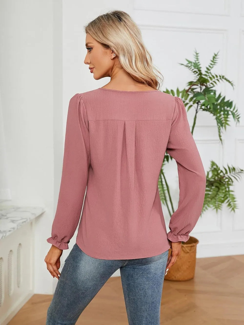 Woman wearing a dusty pink notched neck long sleeve blouse with flounce cuffs styled with light-wash jeans.