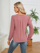 Woman wearing a dusty pink notched neck long sleeve blouse with flounce cuffs styled with light-wash jeans.