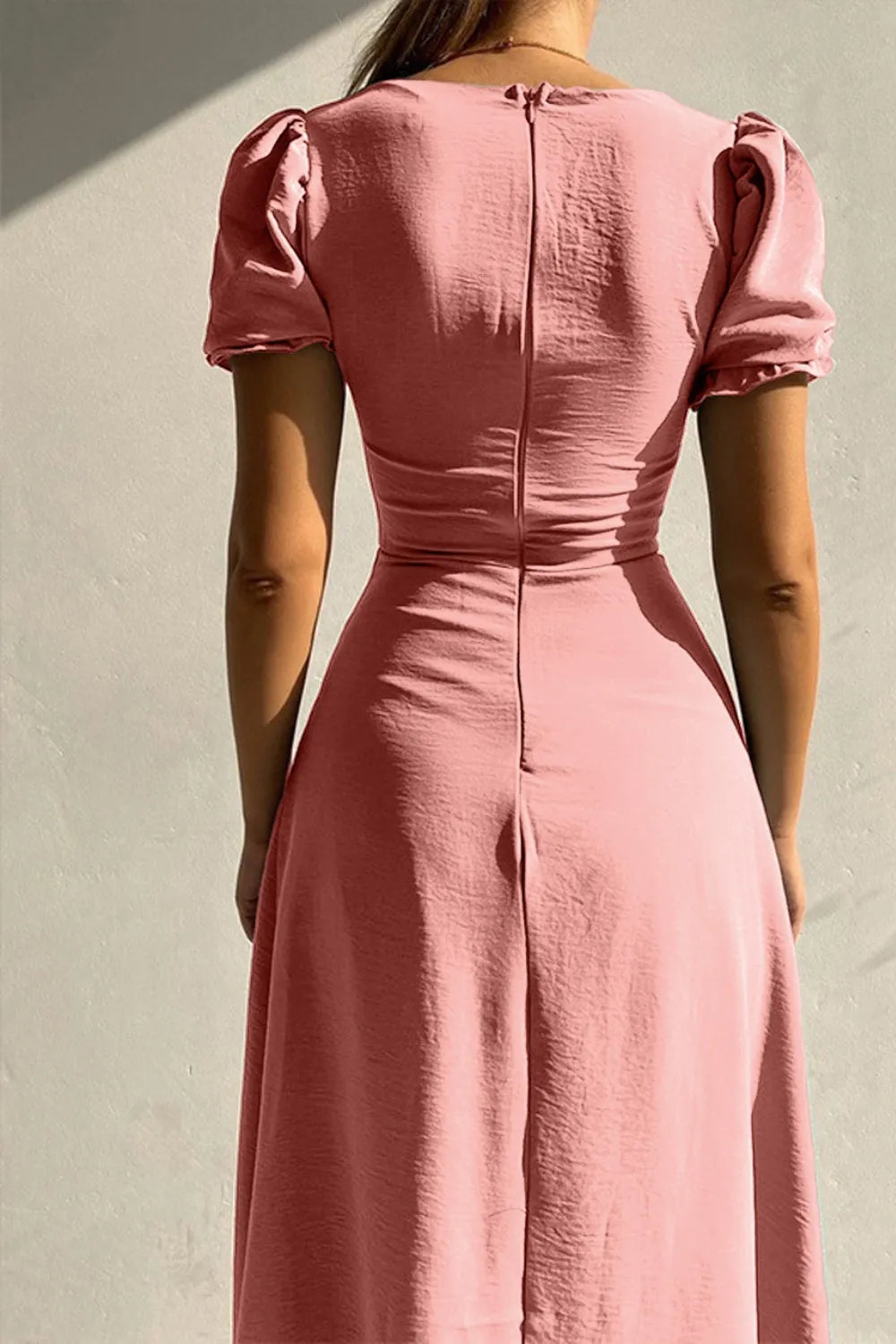 Woman wearing a dusty pink sweetheart-neck midi dress with puff sleeves, ruched detailing, and a button-front slit.