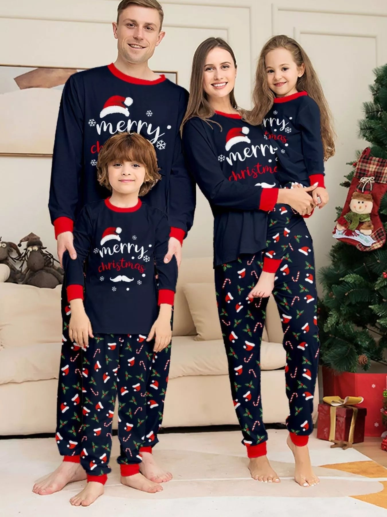 Family of four wearing matching navy blue Merry Christmas pajamas with red trim and festive printed pants beside a Christmas tree.